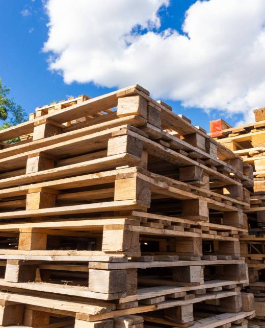 Piles of stacked natural wooden shipping pallets. Outside a big stack with big stack of wooden pallets.